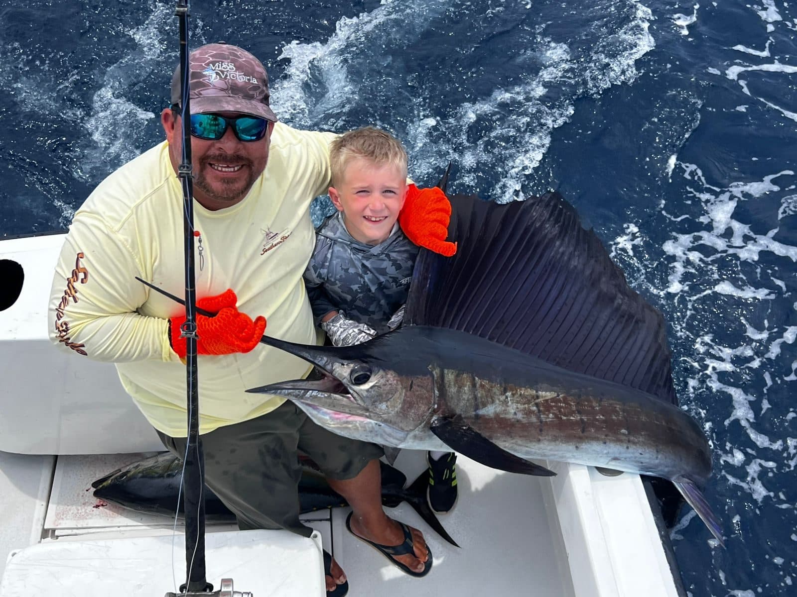 Father and son holding a sailfish aboard the Predator